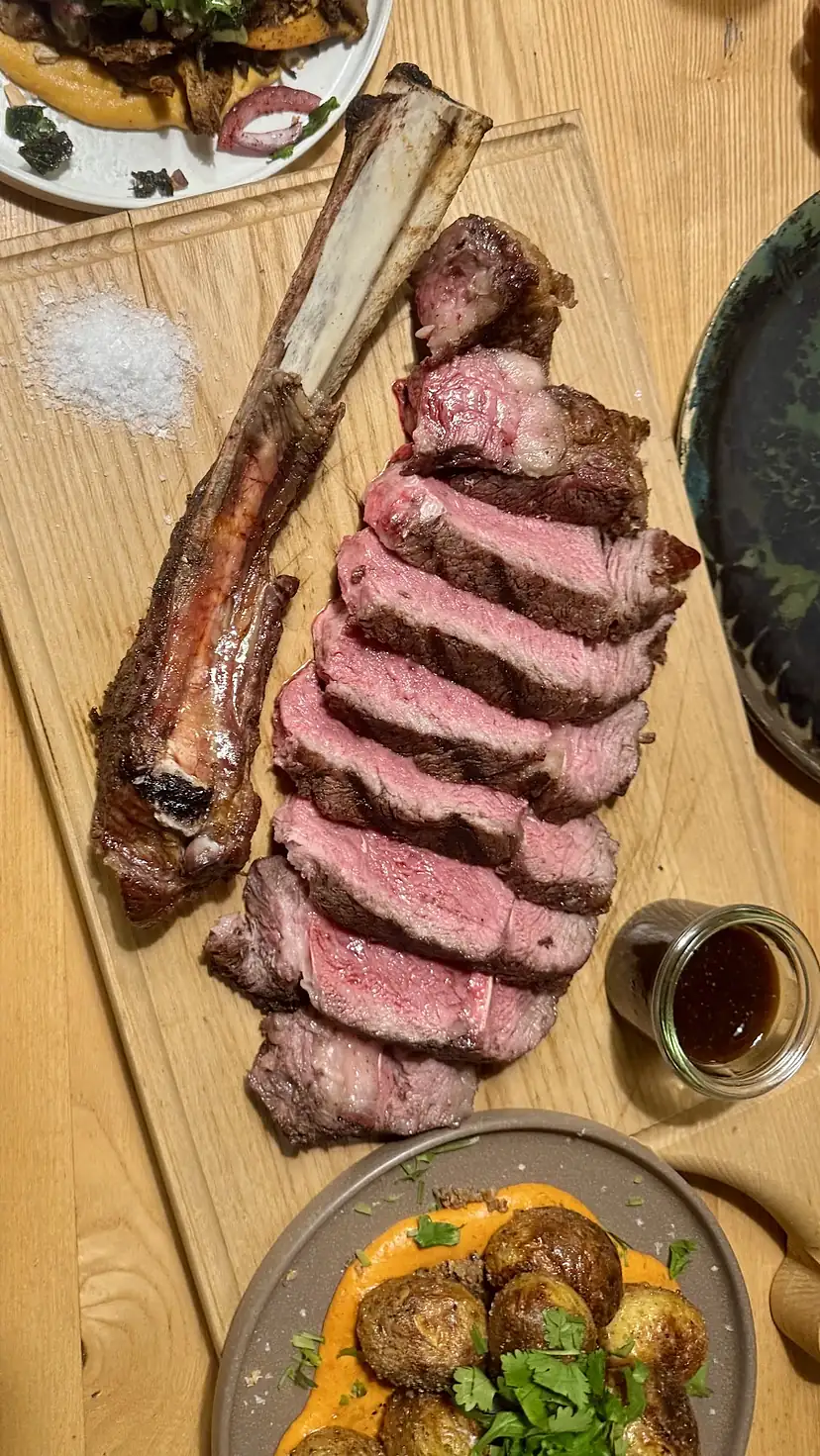 Tomahawk pokrojony na desce, sól, pieczone ziemniaki — stół w Piroman Steak House